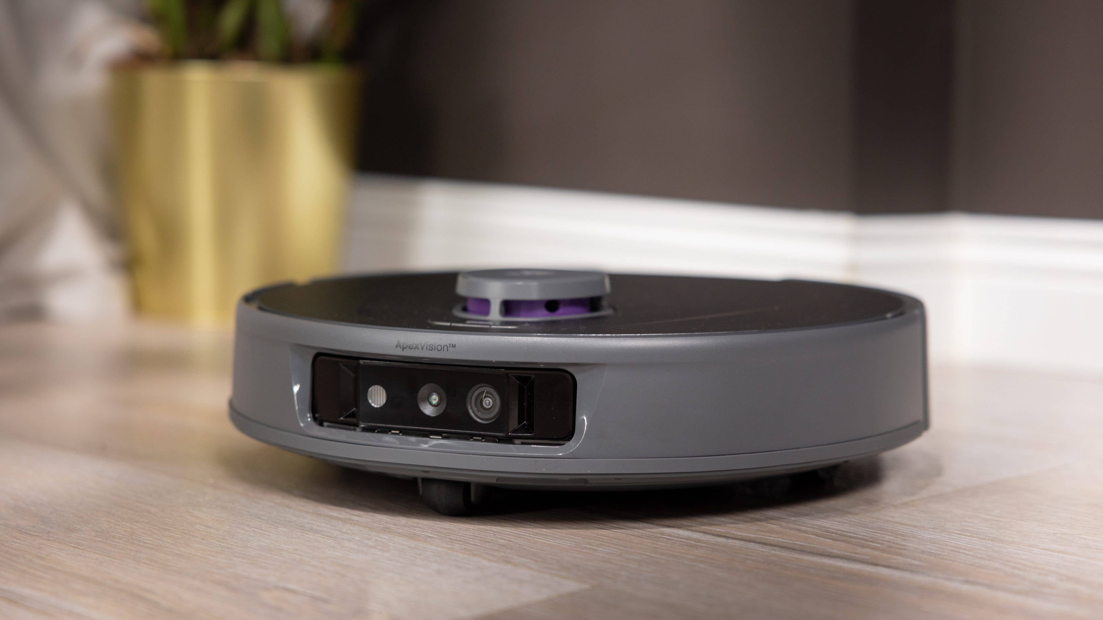 Ein Saugroboter mit elegantem Design steht auf einem Holzboden in der Nähe einer Topfpflanze.