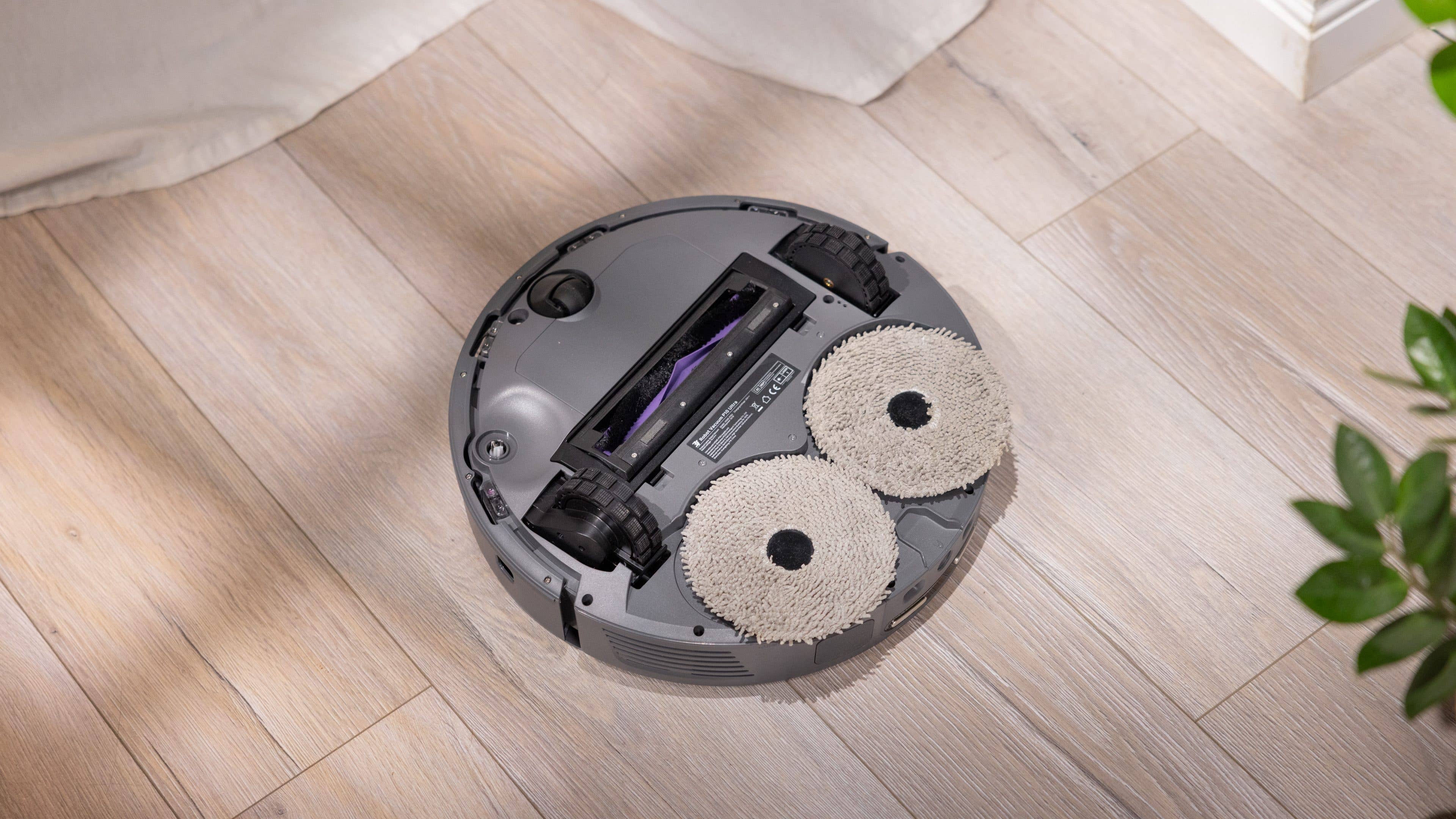 Ein runder robotischer Staubsauger mit zwei Reinigungspads auf einem Holzboden.