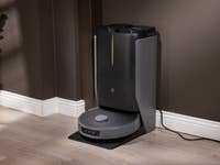 Ein Roboter-Staubsauger an seiner Ladestation gegen eine dunkle Wand.