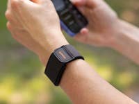 Eine Nahaufnahme eines Handgelenks mit einem Amazfit Helio-Armband, das ein Smartphone hält.