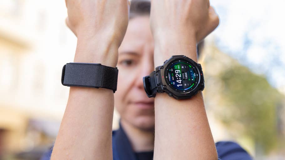 Eine Person zeigt zwei Armbänder, eines ist ein schwarzes Band und das andere eine Amazfit T-Rex Pro 3 Uhr mit Zeit und Statistiken.