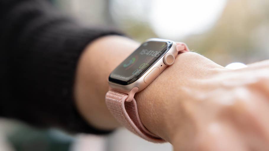 Nahaufnahme einer Apple Watch an einem Handgelenk mit einem pinken Armband, die Uhrzeit und Fitnessmetriken anzeigend.