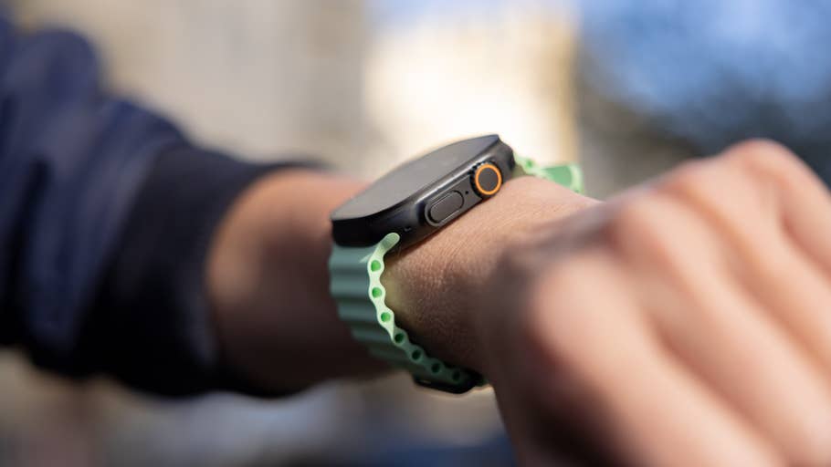 Eine Nahaufnahme einer Apple Watch Series 3 Ultra am Handgelenk einer Person mit grünem Armband.