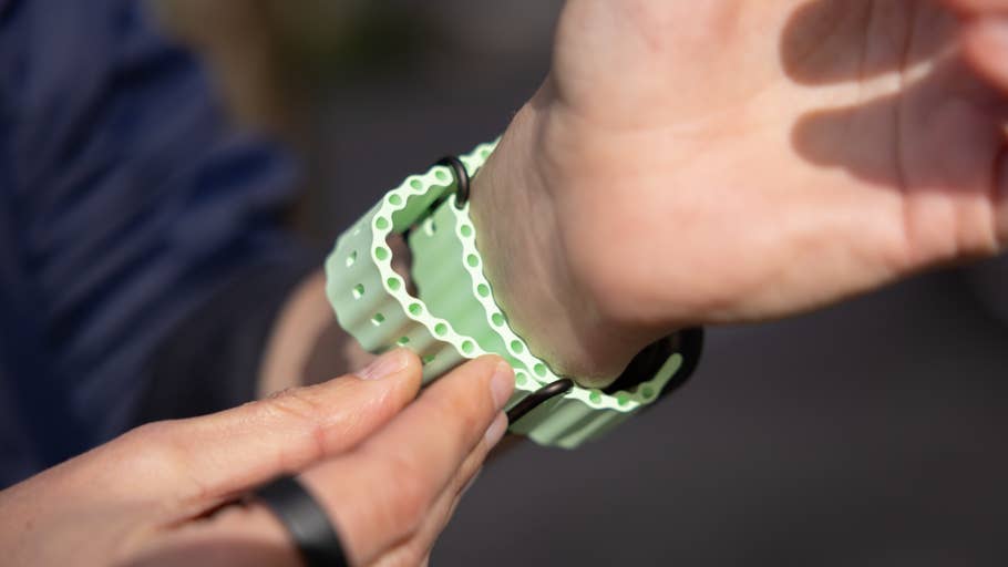 Eine Hand passt ein mintgrünes Armband für eine Apple Watch am Handgelenk an, mit einem dunklen Ring an einem anderen Finger.