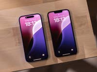 Zwei Apple iPhones, die die Uhrzeit 18:13 auf einer Holzoberfläche anzeigen.