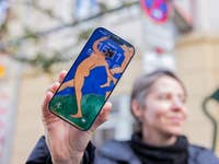 Eine Person hält ein iPhone 17, das ein Kunstwerk als Sperrbildschirm mit der Uhrzeit 15:11 zeigt.