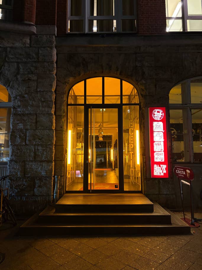 Beleuchteter Eingang eines Gebäudes mit einem Empfangsschild und einem Café-Schild in der Nähe.