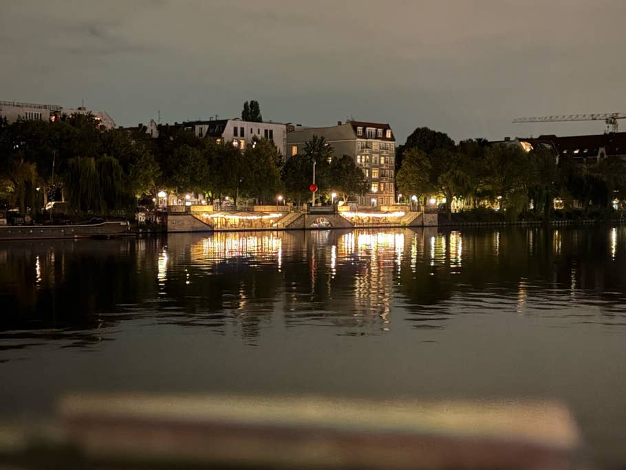 Nachtsicht auf eine Uferpromenade mit beleuchteten Gebäuden und Reflexionen im Wasser.
