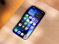 Ein iPhone mit einem bunten App-Layout auf einer Holzoberfläche, das Wetter- und Kalender-Widgets anzeigt.