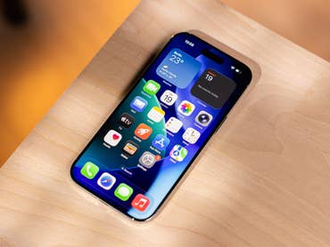 Ein iPhone mit einem bunten App-Layout auf einer Holzoberfläche, das Wetter- und Kalender-Widgets anzeigt.
