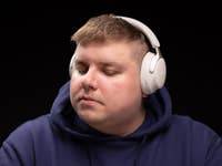 Eine Person trägt Bose QC Ultra Kopfhörer, die Augen geschlossen, wirkt konzentriert und entspannt vor schwarzem Hintergrund.