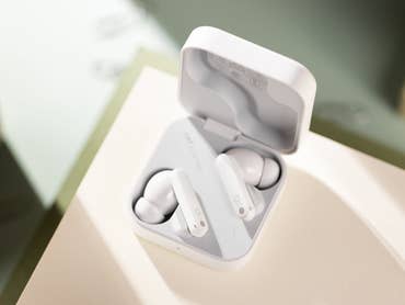 Weiße kabellose Ohrhörer in ihrem Ladeetui auf einer hellen Fläche.