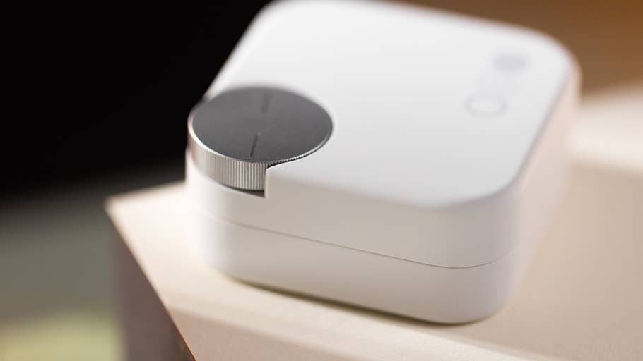 Ein kompaktes weißes Gerät mit einem kreisförmigen Steuerknopf oben, das auf einer hellen Oberfläche liegt.