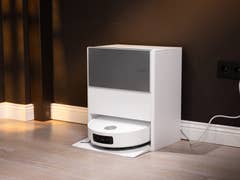 Ein weißer automatischer Staubsauger, angedockt an einer dunklen Wand, mit einem angeschlossenen Stromkabel.