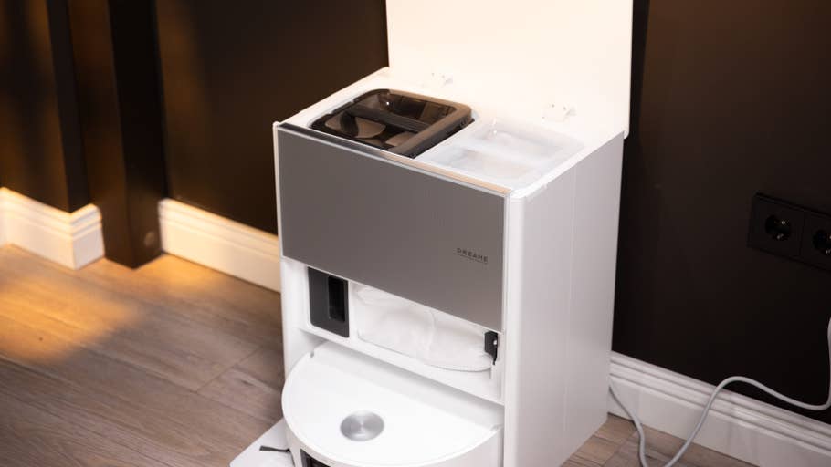 Ein weißes Gerät mit grauem Front, mit Aufbewahrungsfächern und einem runden Boden vor einer dunklen Wand.