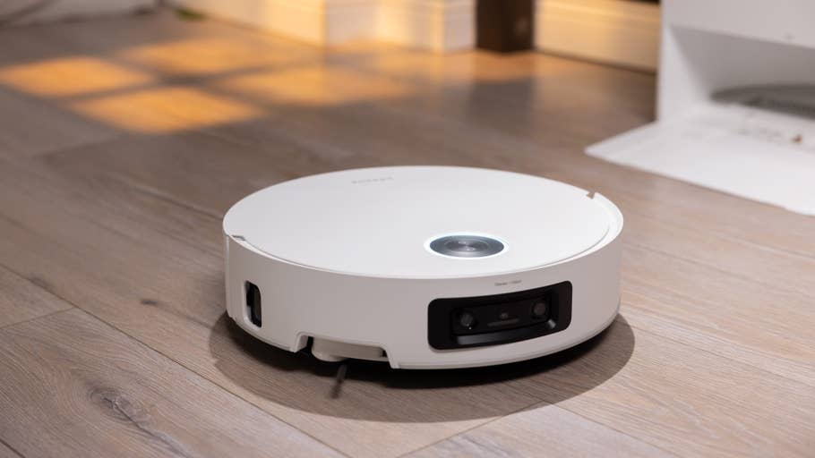 Ein runder, weißer, robotischer Staubsauger auf einem Holzboden mit sanfter Beleuchtung.