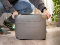 Eine Person, die sich hockt und das tragbare EcoFlow Delta 3 Plus Stromaggregat drinnen hält.