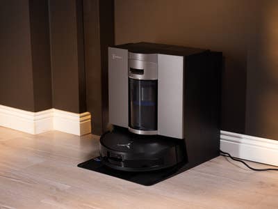 Moderne Ecovacs Deebot X11 Omniclone Saugroboter, angedockt an einer dunklen Wand.