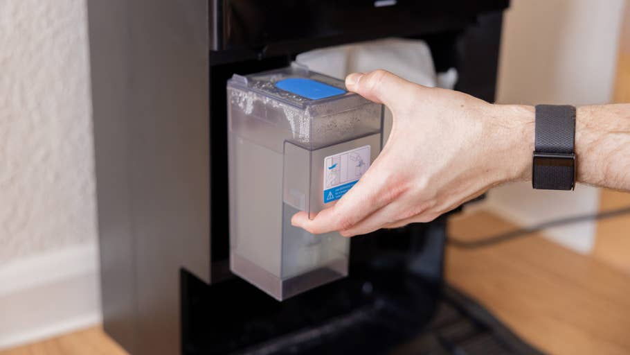 Eine Person entfernt einen Wasserbehälter aus einem schwarzen Gerät, möglicherweise dem Ecovacs Deebot X8 Pro Omni.