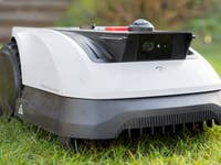 Ein Roboter-Rasenmäher steht auf Gras und verfügt über eine Frontkamera und ein elegantes Design.