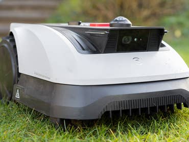 Ein Roboter-Rasenmäher steht auf Gras und verfügt über eine Frontkamera und ein elegantes Design.