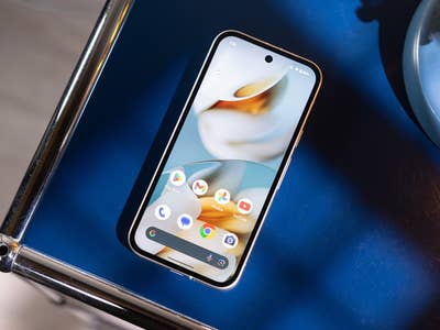 Ein Google Pixel 9a Smartphone auf einer blauen Oberfläche neben einer blauen Lampe.