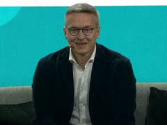 Karsten Wildberger lächelt, während er auf einem Sofa bei einer Konferenz sitzt.