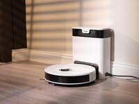 Ein Roboterstaubsauger neben einer Ladestation in einem gut beleuchteten Raum.