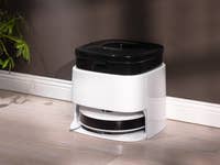 Ein moderner weißer und schwarzer Staubsauger auf einem Holzboden neben einer Pflanze.