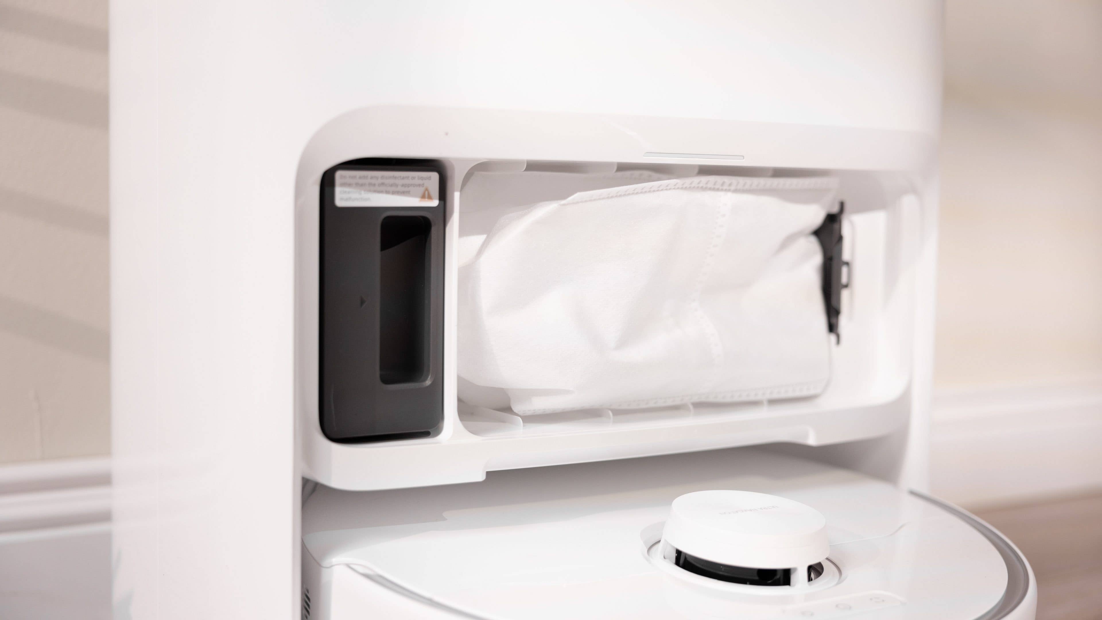 Nahaufnahme des Staubbehälters eines weißen Robotersaugers mit einem abnehmbaren Staubsack.