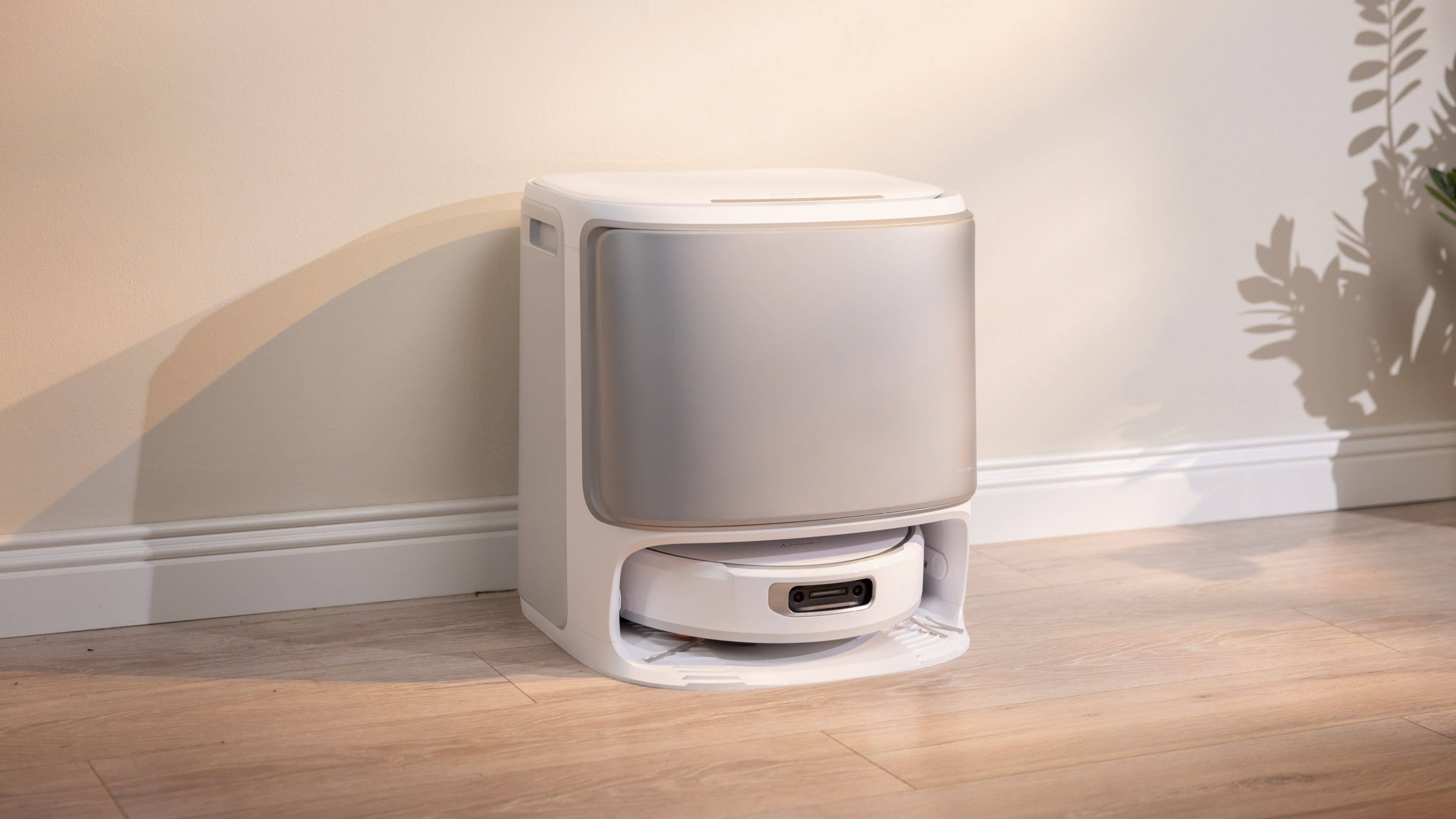 Eine moderne, weiße automatische Katzenkiste auf einem Holzboden vor einer hellen Wand.