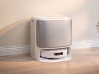 Eine moderne, weiße automatische Katzenkiste auf einem Holzboden vor einer hellen Wand.