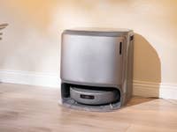 Ein eleganter grauer Saugroboter steht in einem gut beleuchteten Raum an einer Wand.