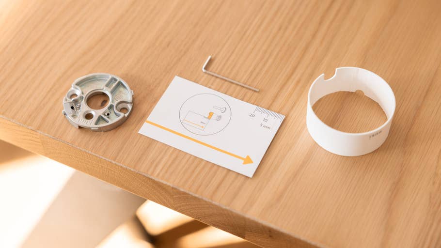 Komponenten für das Nuki Smart Lock Pro auf einem Holztisch: eine Metallbasis, eine Installationsanleitung und eine runde Abdeckung.