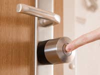 Eine Hand drückt den Knopf eines Nuki Smart Lock Pro, das an einer Holztür angebracht ist.