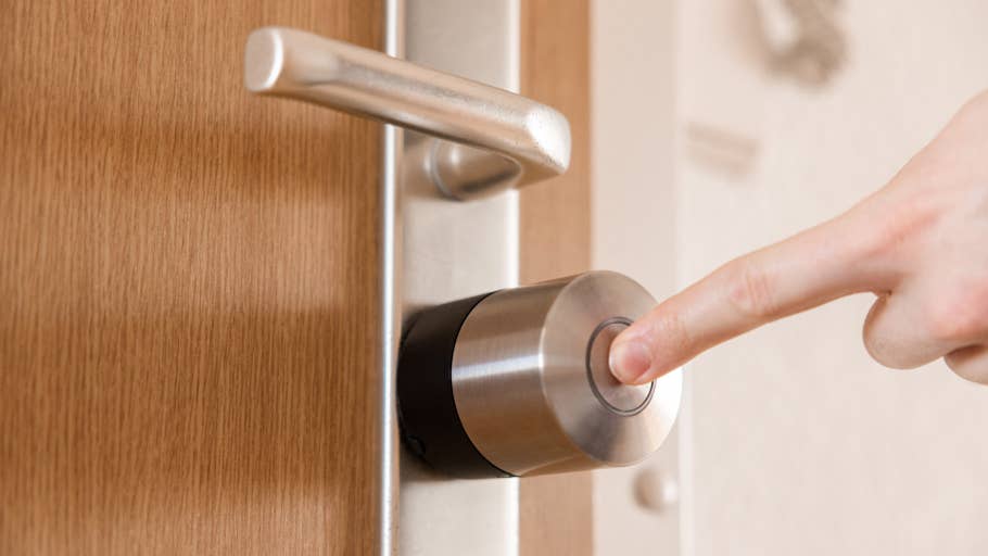 Eine Hand drückt den Knopf eines Nuki Smart Lock Pro, das an einer Holztür angebracht ist.