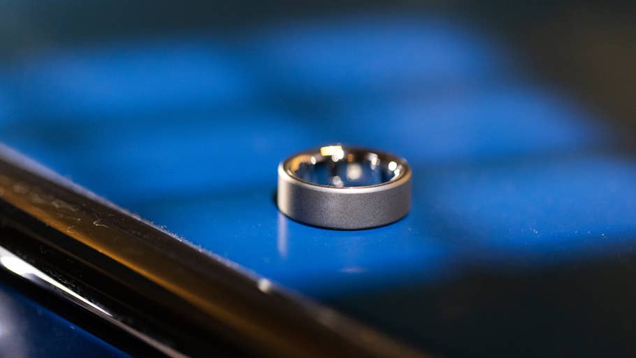 Eine Nahaufnahme eines Oura Rings auf einer blauen Oberfläche, die sein elegantes Design zeigt.