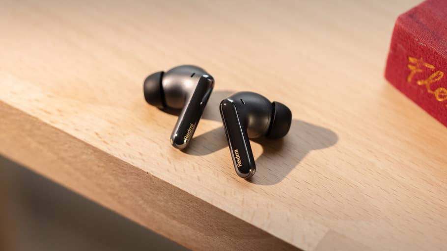 Schwarze Redmi Buds 6 Pro liegen auf einer Holzoberfläche neben einem roten Buch.