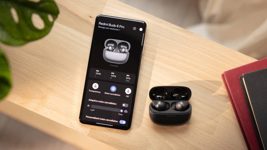Redmi Buds 6 Pro auf dem Handy-Bildschirm mit dem Ohrhörer-Case auf einer Holzoberfläche.
