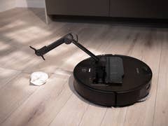 Ein Roborock Saros Z70 Saugroboter auf einem Holzboden neben einem Tuch.