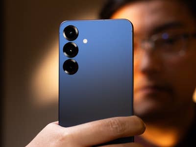 Eine Person hält ein Samsung Galaxy S25 Plus Smartphone mit einem blauen Farbverlauf und drei Kameralinsen.