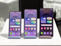 Drei Samsung Galaxy S25-Handys auf Ständern, die verschiedene Startbildschirm-Layouts zeigen.