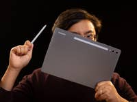 Person hält ein Samsung Galaxy Tab S10+ und einen Stylus vor einem dunklen Hintergrund.