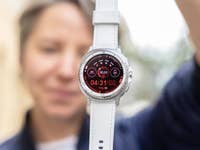 Eine Person hält eine Samsung Galaxy Watch 8 Classic, die ein rotes Interface mit Uhrzeit und Fitnessstatistiken zeigt.