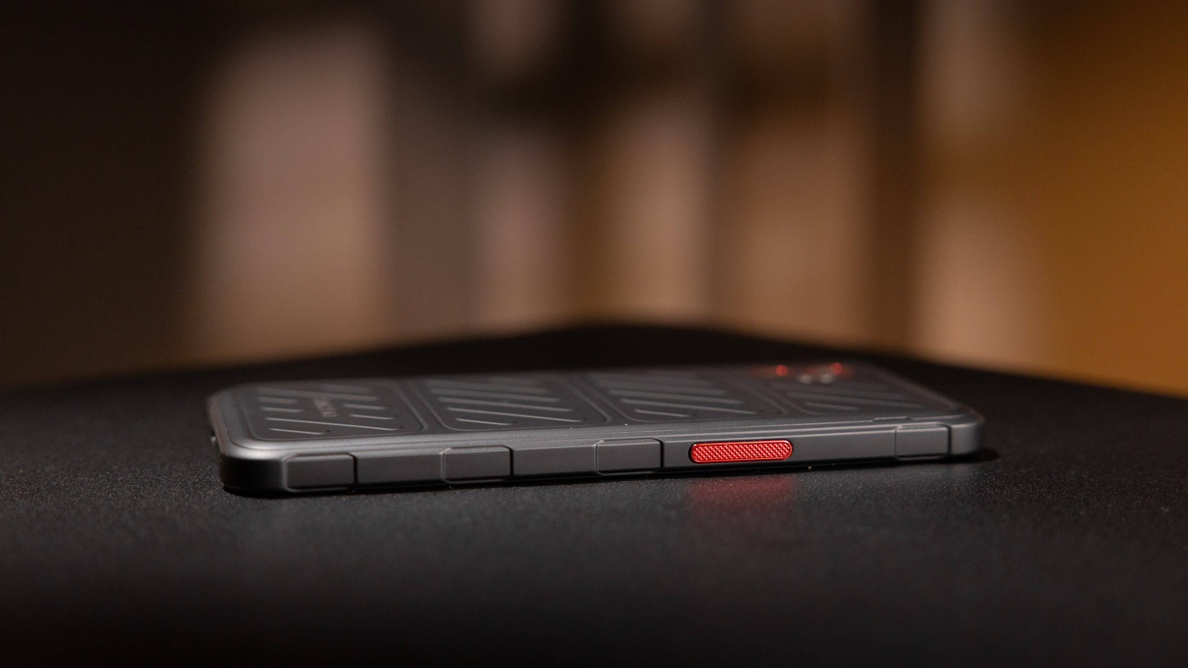 Samsung Galaxy XCover 7 Pro Smartphone auf einer dunklen Oberfläche, mit einer strukturierten Rückseite und einem roten Knopf. Samsung Galaxy XCover 7 Pro Smartphone auf einer dunklen Oberfläche, mit einer strukturierten Rückseite und einem roten Knopf.