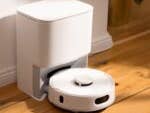 Ein weißer Staubsauger-Roboter neben einer Ladestation auf Holzboden.
