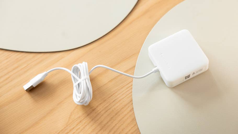 Ein weißes SwitchBot Lock Ultra Touch Combo-Gerät mit einem USB-Kabel auf einer Holzoberfläche.