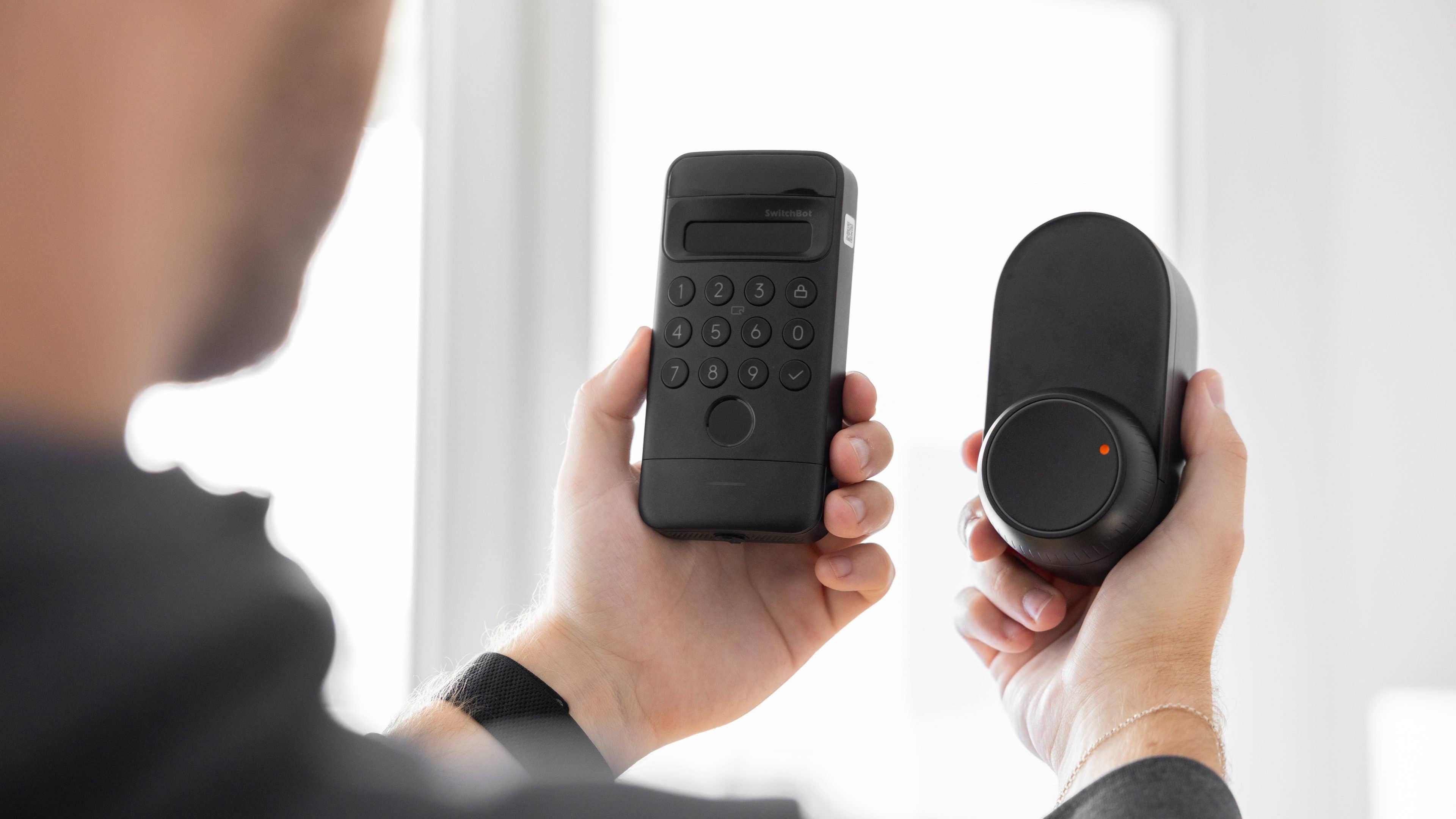 Eine Person hält ein SwitchBot Ultra Touch-Tastatur-Schloss und ein Smart-Lock-Gerät in den Händen.