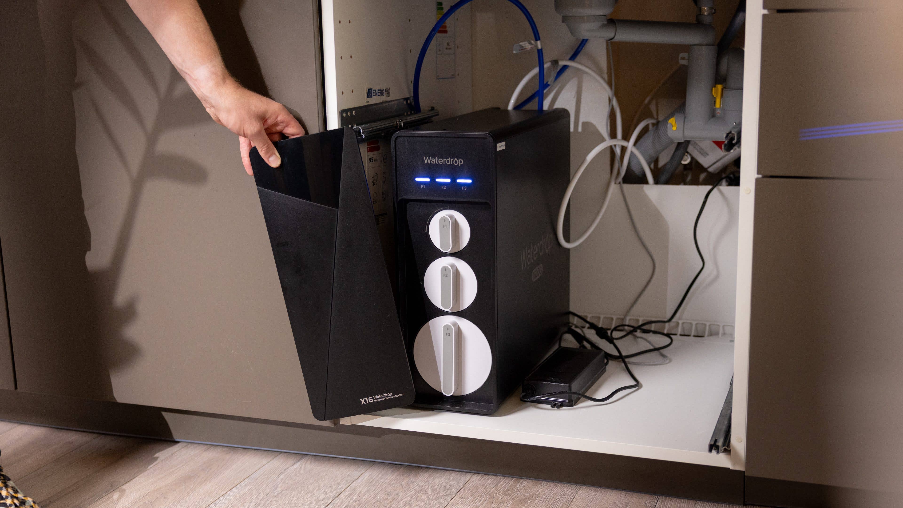 Eine Hand hält einen schwarzen Wasserfilter, der an einer Waterdrop-Einheit unter der Küchenspüle befestigt ist.