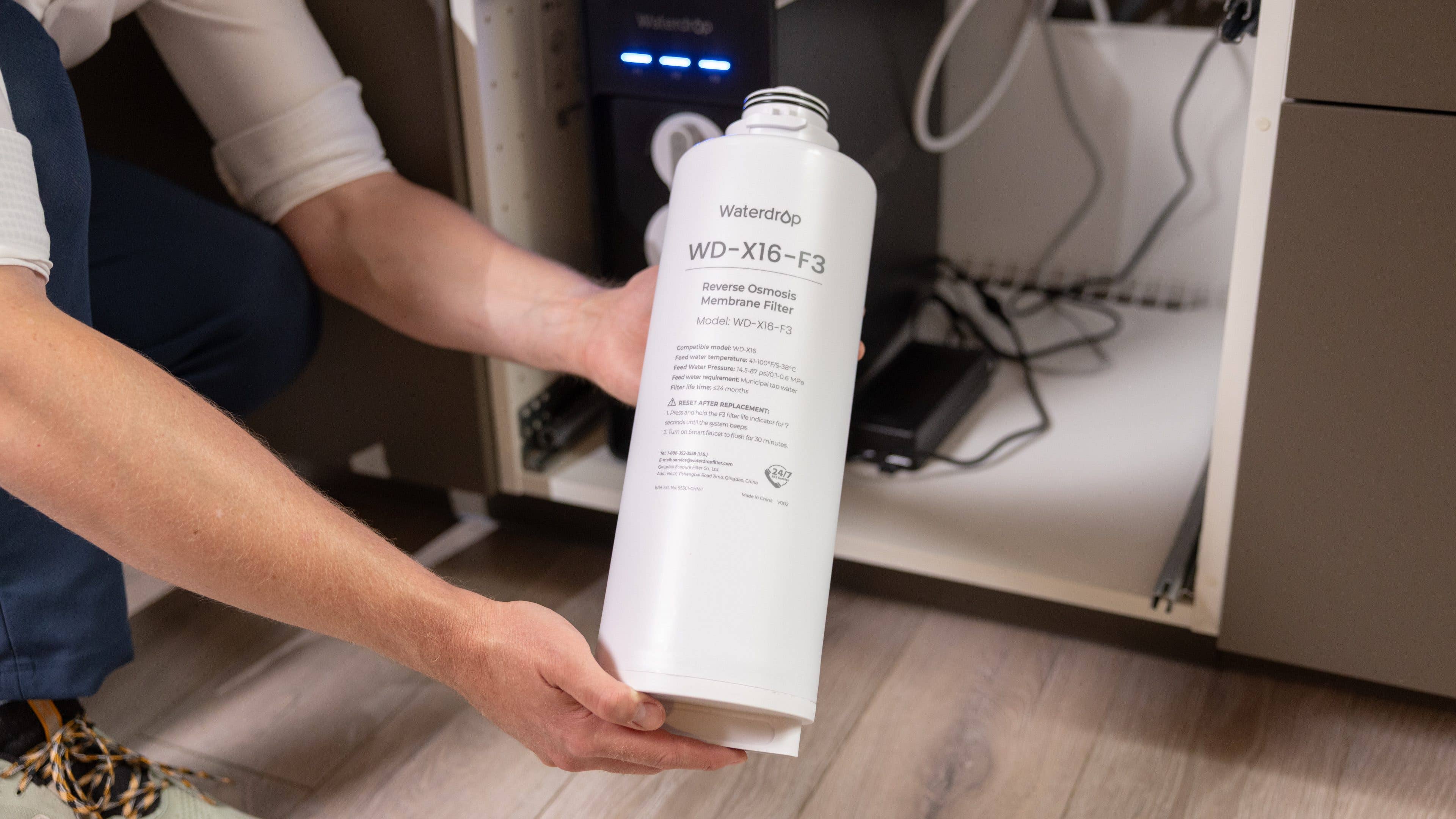 Eine Person hält einen Waterdrop WD-X16-F3 Umkehrosmosefilter in einem Küchenschrank.